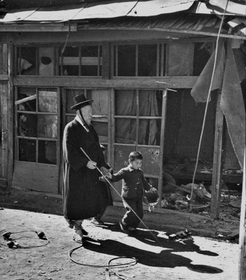Balaca uşaq müharibədə dağıdılmış küçələrdə kor qocanı aparır. Koreya müharibəsi, 1951-ci il